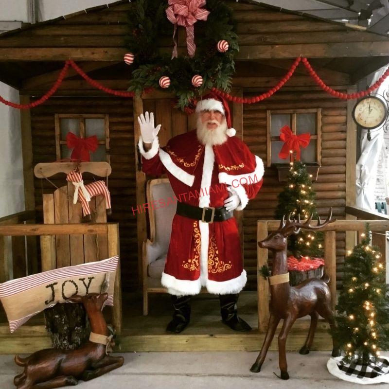 Hire Santa Miami real-bearded Santa waving hello from a Christmas cabin set